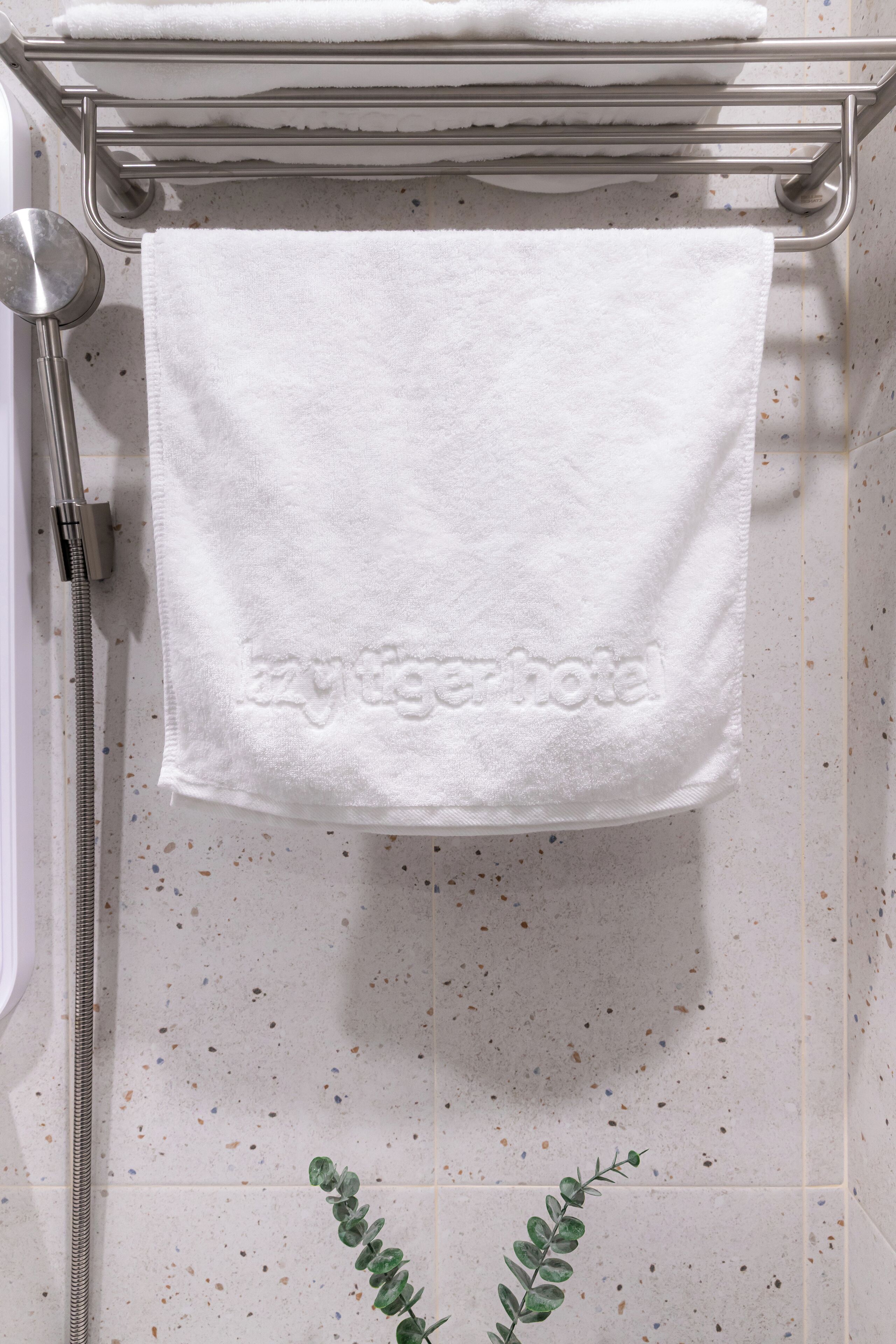 Baño con ducha, toallero y una toalla de spa con el logotipo de "Baytigerhotel" grabado.