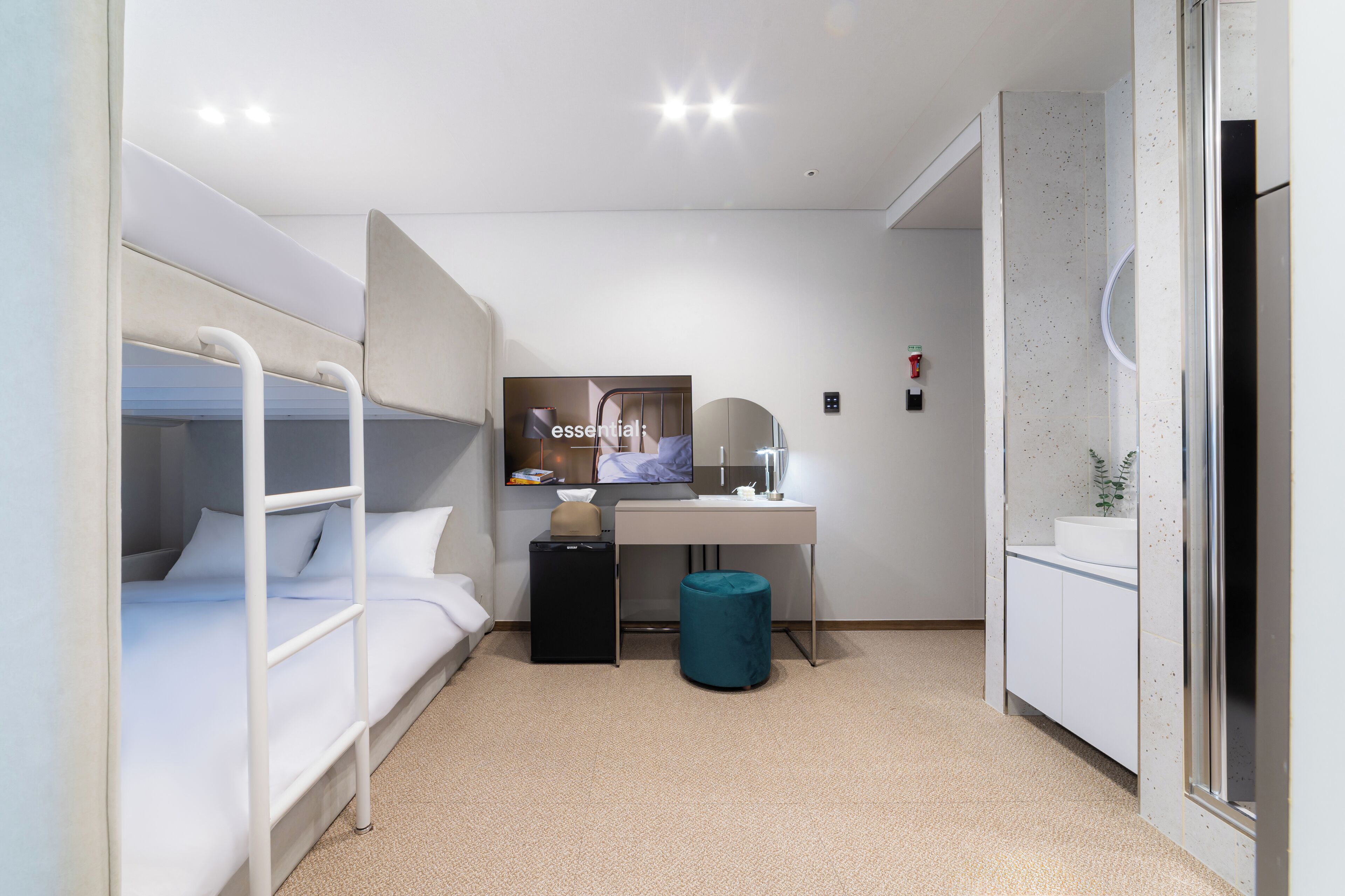 A compact hotel room with bunk beds, a desk, a small trash bin, and a sink.