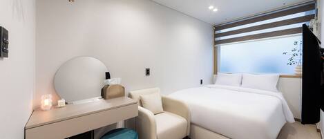 Une chambre d’hôtel moderne équipée d’un lit, d’un bureau, d’une chaise, d’une petite poubelle et d’une fenêtre avec des stores.