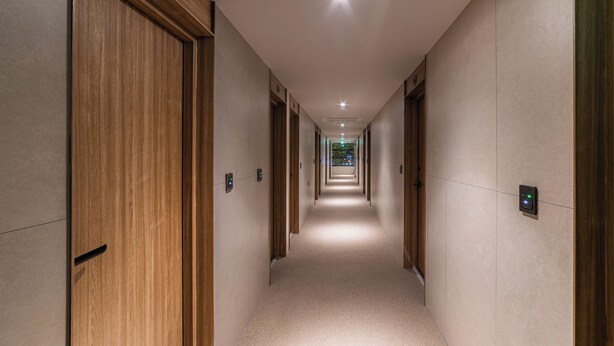 A hotel hallway with wooden doors, a carpeted floor, and a modern light fixture on the ceiling. - Lazy Tiger Hotel (Seoul)