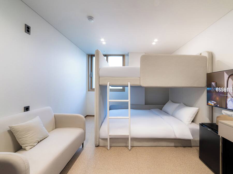 Habitación pequeña con una cama litera, un sofá, un escritorio y un televisor.