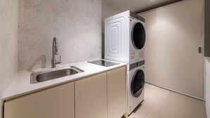 A compact kitchen with a built-in washer and dryer, a stainless steel sink, and a speckled backsplash. - Lazy Tiger Hotel (Seoul)