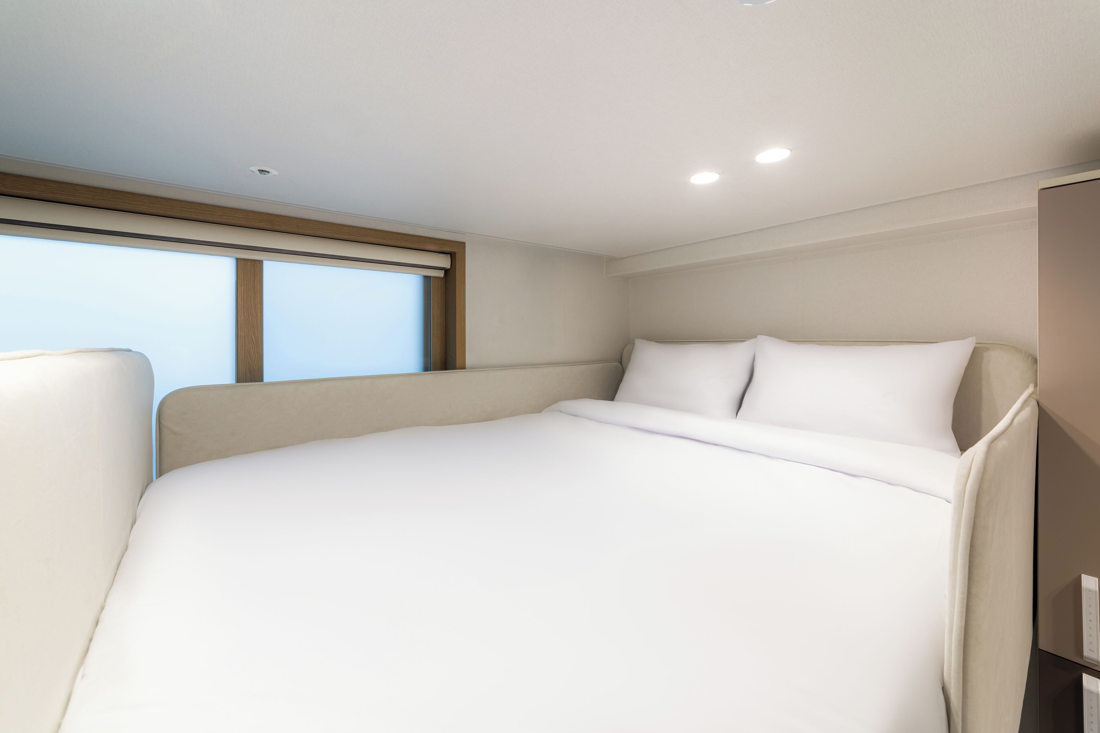 Ein modernes Hotelzimmer mit einem großen Bett, einem Fenster mit Jalousien und einem integrierten Schreibtisch.