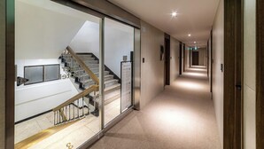 A modern hotel corridor with a glass wall, a staircase, and a wooden door. - Lazy Tiger Hotel (Seoul)