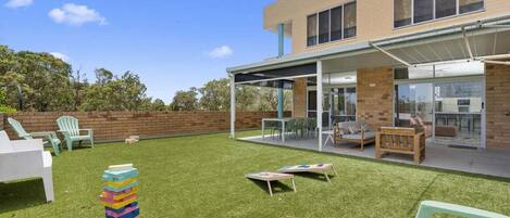 A modern building with a covered patio area, outdoor seating, and a grassy lawn.