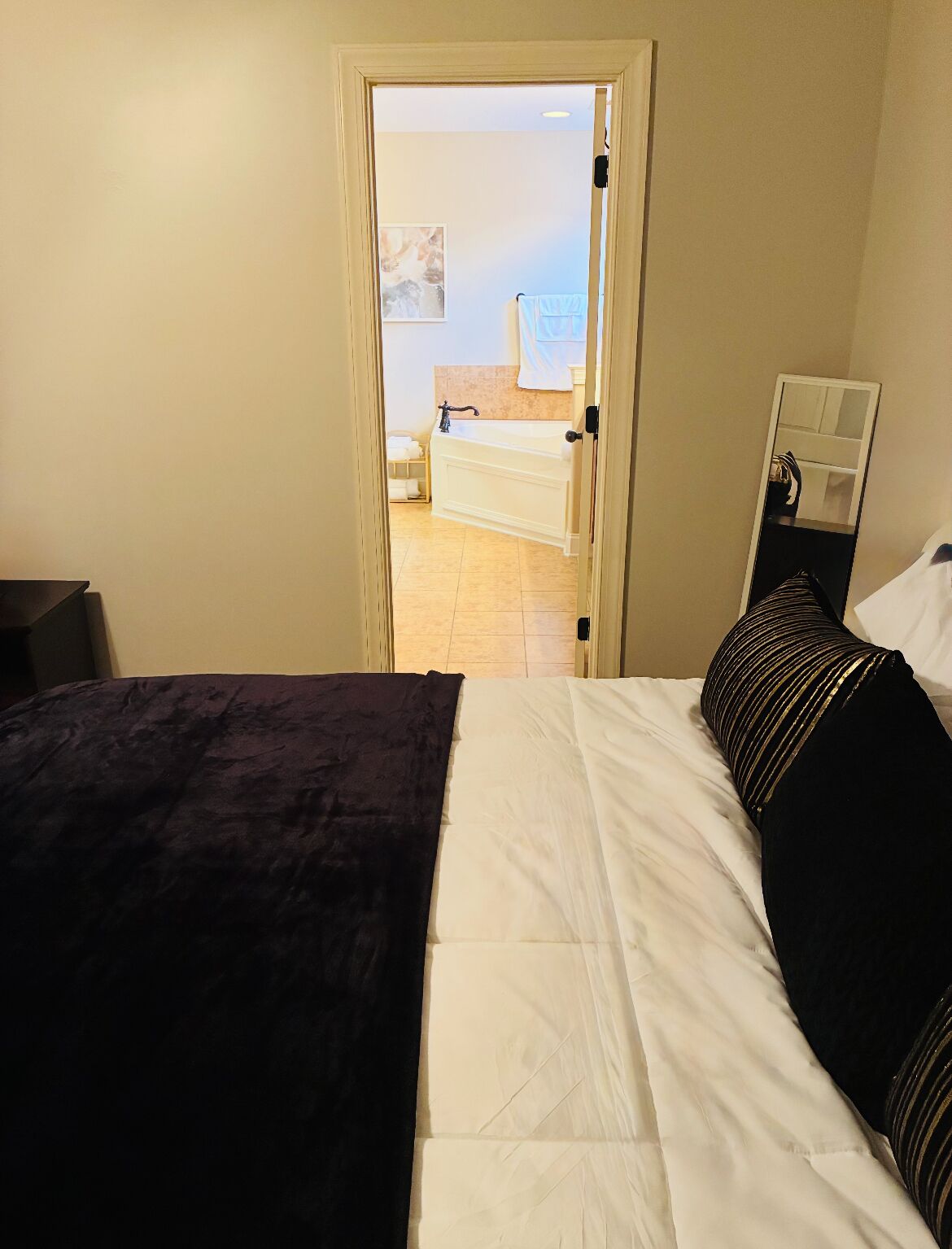 Une chambre à coucher avec un lit, une table de chevet et une vue sur une salle de bain équipée d’une baignoire et d’un porte-serviettes.