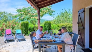 A covered outdoor dining area with stone flooring, a table set for a meal, and chairs. - Villa in Pyrenees With Pool & Terrace (Quillan)