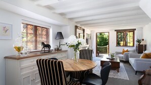 A dining area with a round table, striped chairs, a vase with flowers, and a window with blinds. - Relax, Explore, Unwind — Coastal Comfort at The Little Monaco (Nelson)