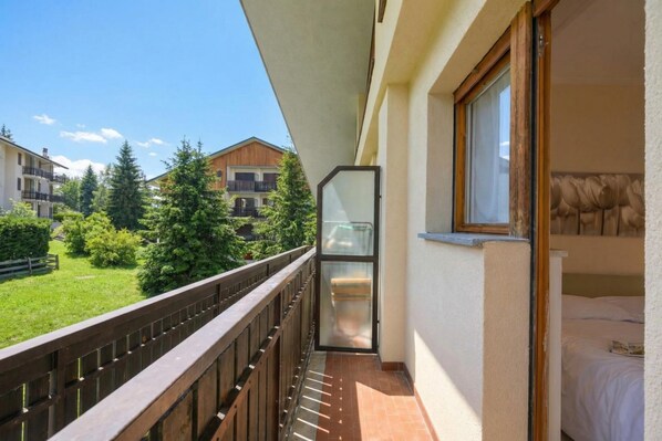 Un balcon avec une balustrade en bois, une porte-fenêtre coulissante et un lit doté d’une tête de lit blanche.