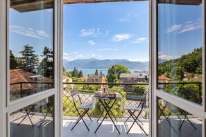 A balcony with a table and chairs, overlooking a mountainous landscape and a body of water. - La Caravella: Stresa Lake & Islands View Balcony (Stresa)