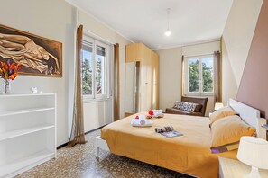 Een hotelkamer met een bed, nachtkastje, lamp, raam en een schilderij aan de muur.