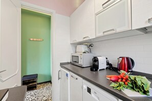 A compact kitchen with white cabinets, a microwave, a toaster, a kettle, and fresh vegetables on the counter. - La Caravella: Stresa Lake & Islands View Balcony (Stresa)