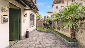 A courtyard with a stone pathway, a green door, a wall-mounted light fixture, and a statue. - La Caravella: Stresa Lake & Islands View Balcony (Stresa)
