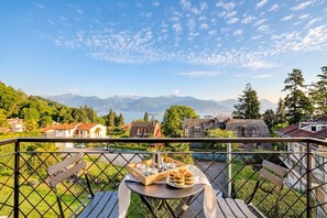 A balcony with a table set for tea, overlooking a scenic view of mountains and a lake. - La Caravella: Stresa Lake & Islands View Balcony (Stresa)