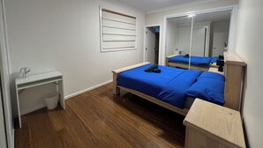 A bedroom with a wooden floor, a bed with blue bedding, a bedside table, a mirror, and a wall-mounted shelf. - 7 mins walking to Bus Station, 5 mins driving to epping train station (Beecroft)