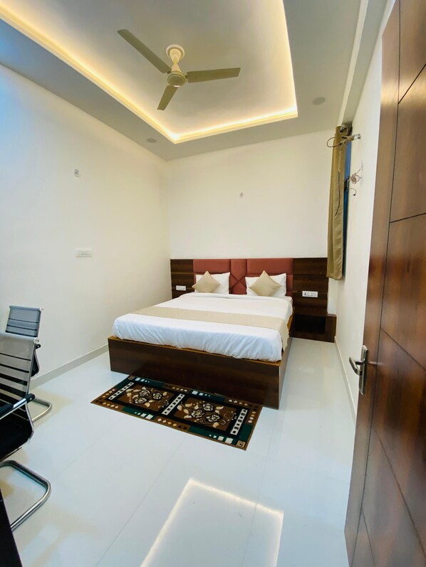 A bedroom with a bed, a desk, a chair, a ceiling fan, and a door. - Hotel Taj Silver Palace (Agra)