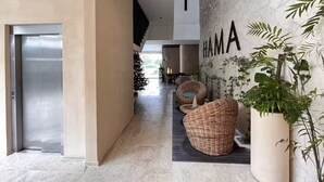 Un intérieur moderne comprenant un couloir, un mur orné du mot « HAMA » en grandes lettres, des meubles en osier et une plante en pot.