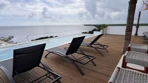 Une terrasse en bois avec des chaises longues donnant sur une piscine et l’océan.