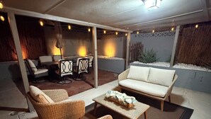 Un área de patio al aire libre con mobiliario de mimbre, un sofá blanco y una mesa con un centro de mesa floral.