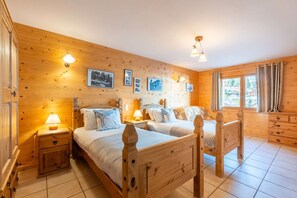 Une chambre aux murs lambrissés, avec deux lits, des lampes de chevet et une fenêtre avec des rideaux.