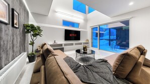 A modern living room with a sofa, a coffee table, and a flat-screen TV on a white wall. - THE VELLMORE (Asahikawa)