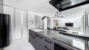 A modern kitchen with a large island, built-in appliances, and a dining area with a TV. - THE VELLMORE (Asahikawa)