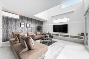A modern living room with a large flat-screen TV, a sectional sofa, and a coffee table. - THE VELLMORE (Asahikawa)