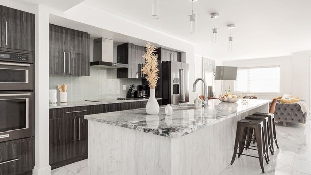 A modern kitchen with dark wood cabinets, a marble island, stainless steel appliances, and a large window providing natural light. - Lux New House by UA/Train/Rogers Place/Hospital/Ravine/AC/D-garage/sleep 12 (Edmonton)