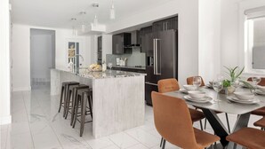 A modern kitchen with a marble island, stainless steel appliances, and a dining area with a table set for four. - Lux New House by UA/Train/Rogers Place/Hospital/Ravine/AC/D-garage/sleep 12 (Edmonton)