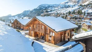 A wooden chalet with a snow-covered roof, situated in a mountainous area with other buildings and a clear sky. - Bleriot T : demi-chalet au pied des pistes (LE GRAND BORNAND)