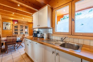 Ein Holzblockhaus-Innenraum mit einer Küche, die weiße Schränke, ein Waschbecken und ein Fenster mit Blick auf eine verschneite Landschaft zeigt.