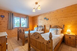 Ein Schlafzimmer in einer Holzhütte mit zwei Betten, einem Nachttisch, einer Kommode und einem Fenster mit Vorhängen.