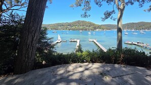 A marina with boats docked, surrounded by trees and hills in the background. - Island escape with private waterfront beach and jetty on Scotland Island. (Scotland Island)