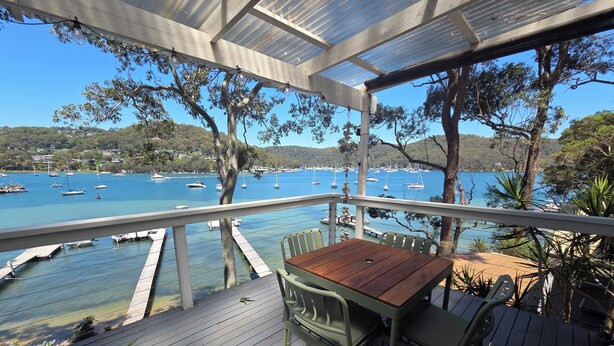 A wooden deck with a table and chairs overlooking a marina with boats. - Island escape with private waterfront beach and jetty on Scotland Island. (Scotland Island)