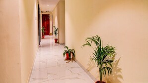 A corridor with marble flooring, potted plants, and a red door at the end. - Collection O The Hastings Club (Kolkata)