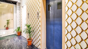 A hallway with a blue door, a patterned wall, and potted plants. - Collection O The Hastings Club (Kolkata)