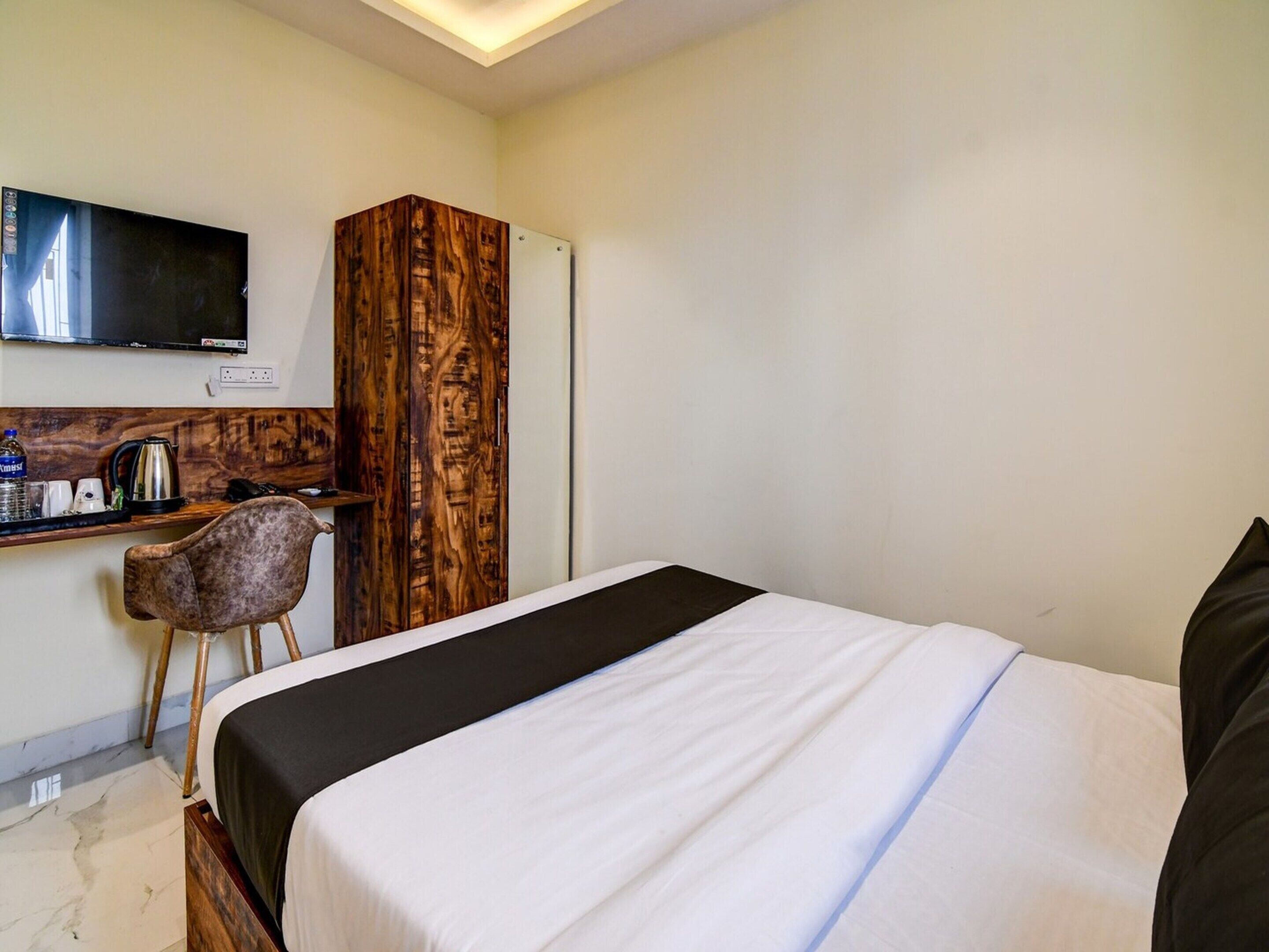 A hotel room with a bed, a wooden wardrobe, a desk with a chair, a television, and a coffee maker.