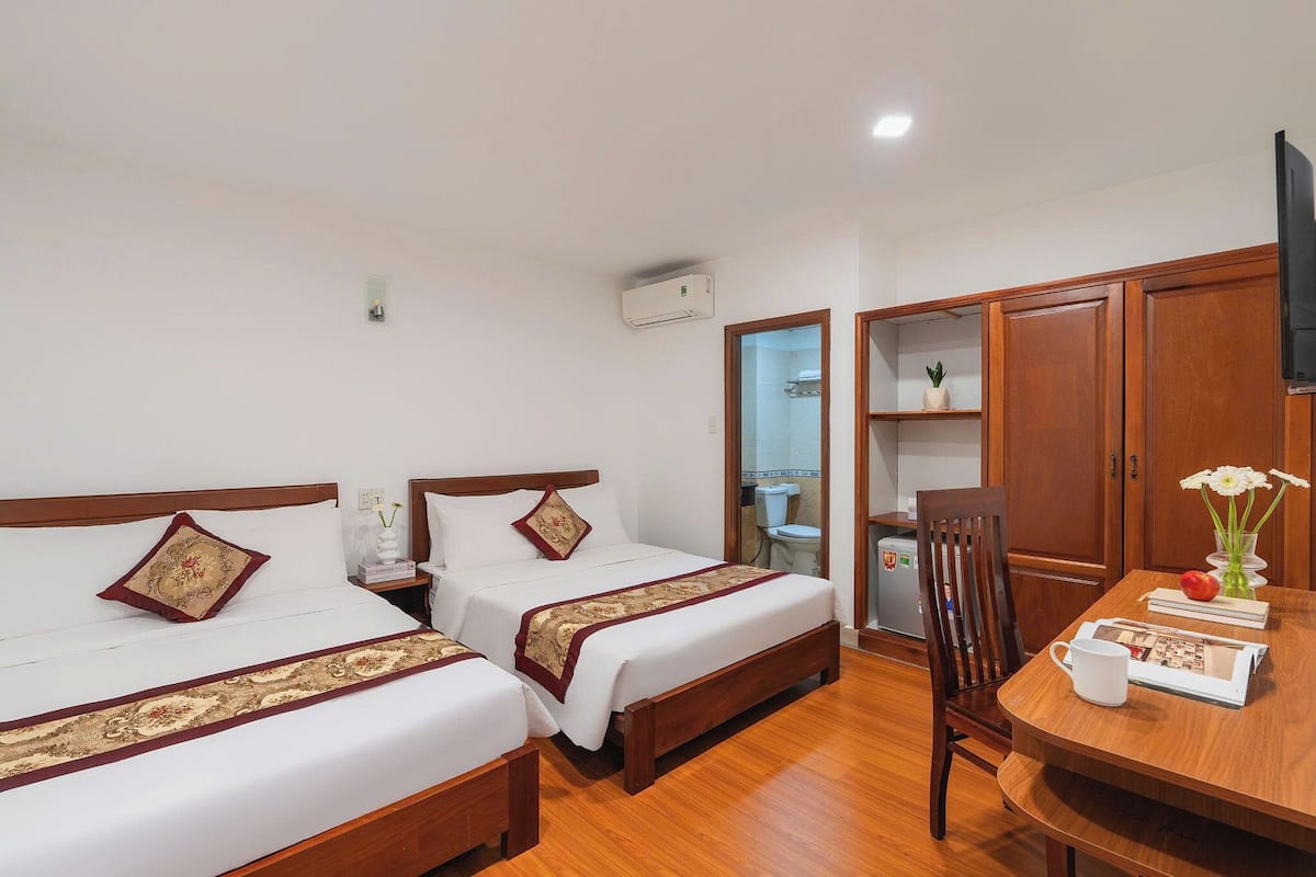 Habitación de hotel con dos camas, una mesa de comedor de madera, una silla, un televisor y un baño visible a través de una puerta abierta.