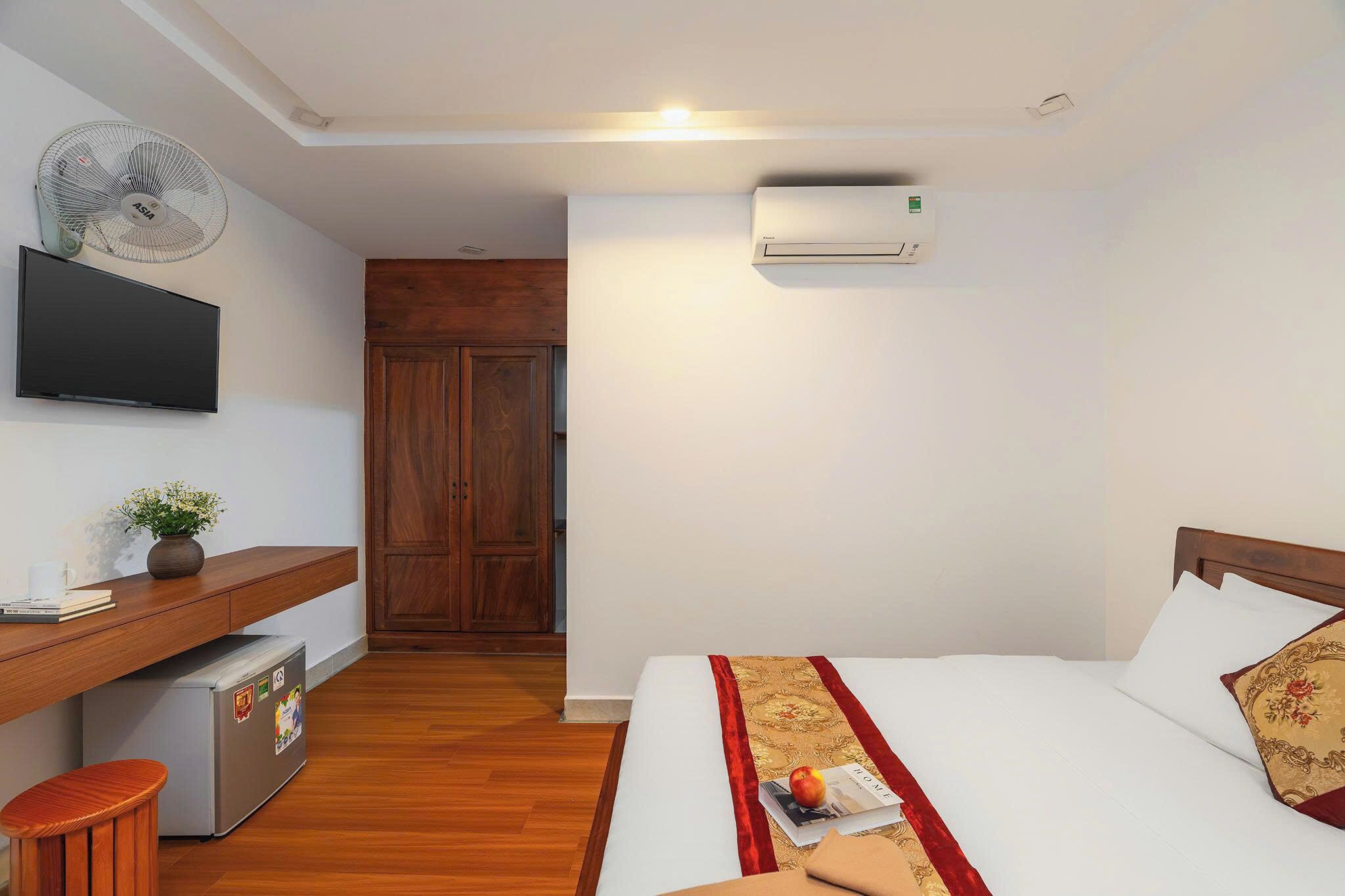 A hotel room with a bed, a desk with a computer, a TV, and an air conditioning unit.