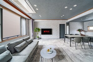A modern living room with a sofa, coffee table, and a TV screen displaying 'NETFLIX'. - THE HALCYON (Sapporo)