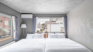 Habitación de hotel con una cama grande, ventana con cortinas, aire acondicionado y vistas a edificios.