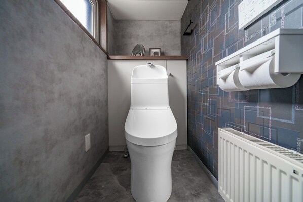 A modern bathroom with a toilet, a towel dispenser, and a radiator. - THE HALCYON (Sapporo)