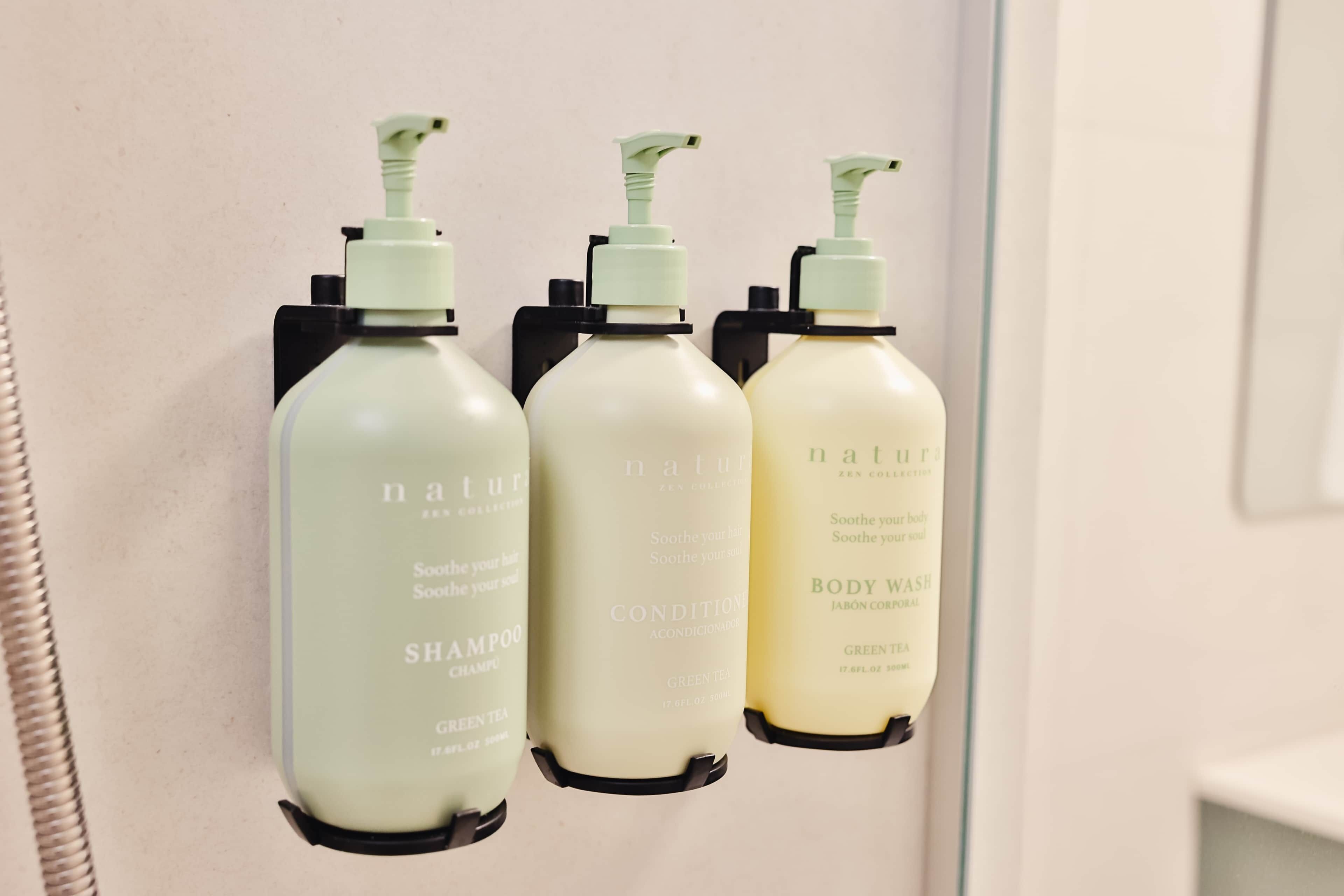 Trois bouteilles de shampoing et de gel douche sont posées sur un mur.