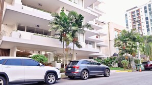 Un immeuble à plusieurs étages doté de balcons, avec des voitures garées et des palmiers.