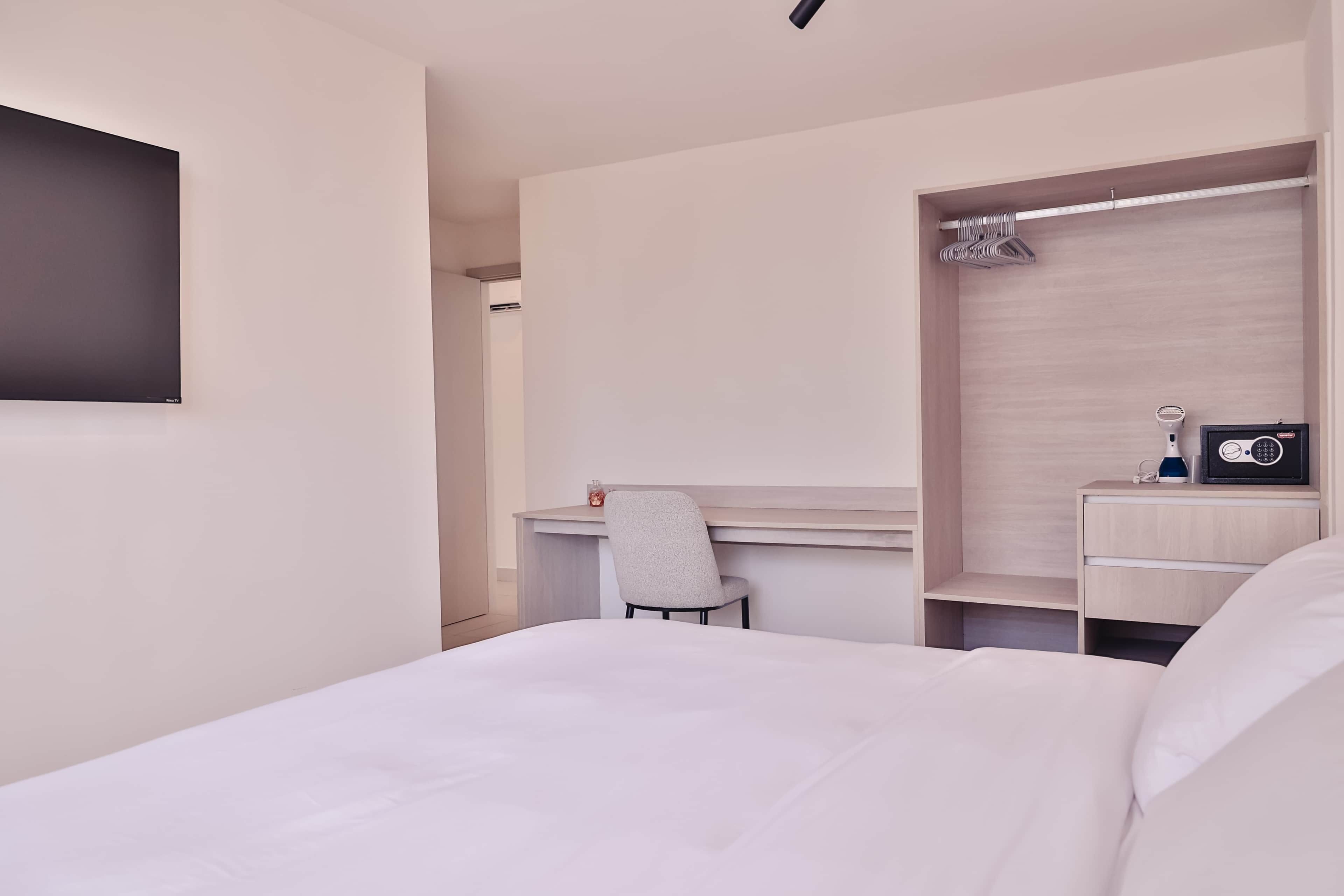 Une chambre d’hôtel moderne équipée d’un lit, d’un bureau, d’une chaise, d’une armoire et d’un téléviseur à écran plat.