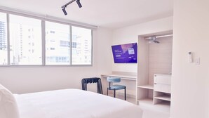 A modern hotel room with a large bed, a desk with a chair, a TV, and a built-in shower area. - Apartment 6B Doña Raquel in Panama City (Panama City)