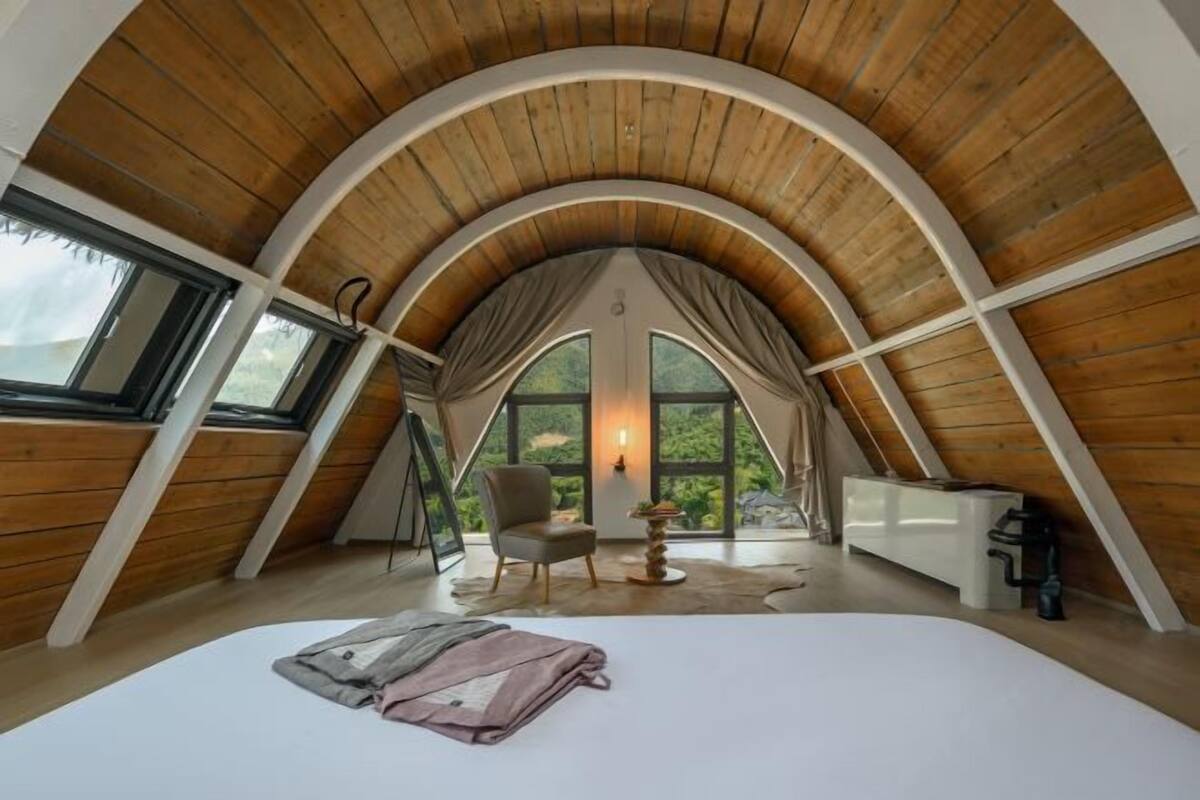A high-ceilinged attic bedroom with a bed, a chair, and a table.