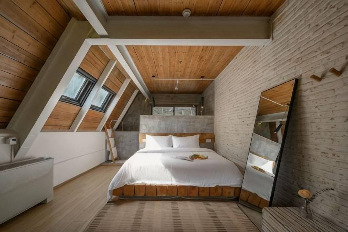 A bedroom with a sloped ceiling, a bed, a large mirror, and a view of the sky through skylights.