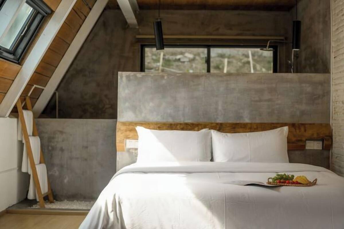 A bedroom with a sloped ceiling, a bed with white linens, a small window, and a wooden ladder.