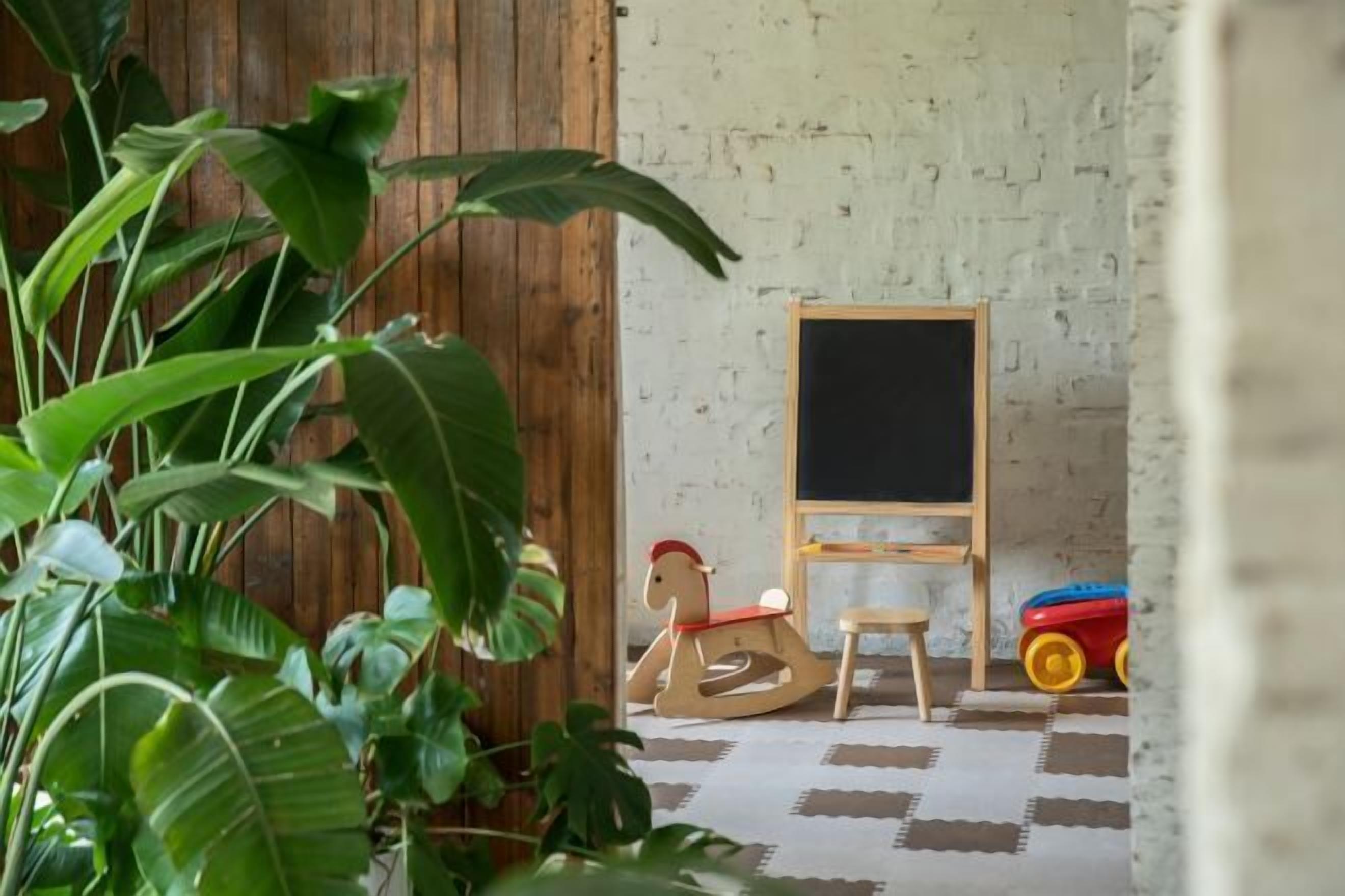 A room with a wooden rocking horse, a small wooden chair, and a blackboard on a wall.